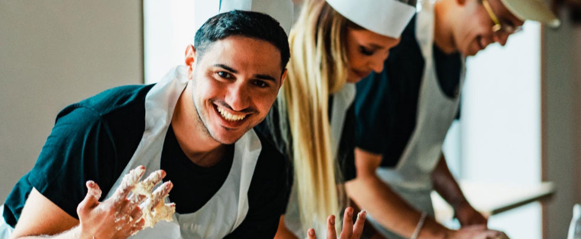 Three happy people kneading dough together in a kitchen, wearing aprons and chef hats.